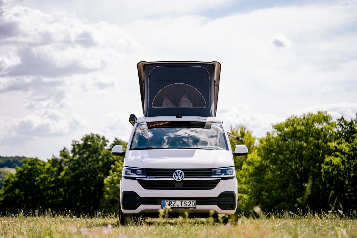 VW T6.1 von vorn mit geöffnetem Aufstelldach auf einer Wiese